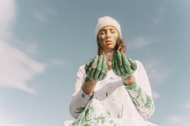 Young woman looking down on her green painted hands - ERRF02386