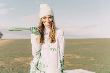 Junge Frau mit grüner Farbe an den Händen, hält einen Stock und lacht - ERRF02390