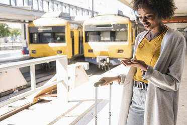 Smiling young woman with earphones and smartphone at platform - UUF19739