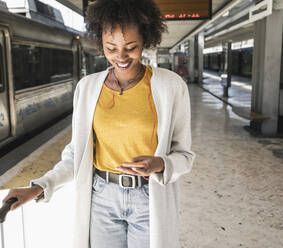 Smiling young woman with earphones and smartphone at platform - UUF19740