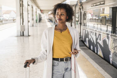 Young woman with earphones and smartphone at platform looking around - UUF19745