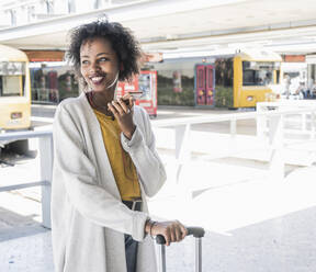 Happy young woman with earphones using smartphone at station platform - UUF19749