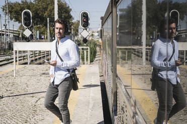 Young man with headphones and smartphone leaving train - UUF19751