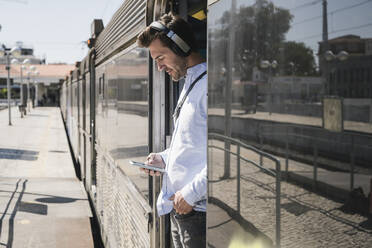 Young man with headphones and smartphone standing in train door - UUF19752