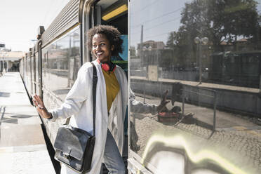 Smiling young woman entering a train - UUF19761