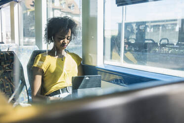 Young woman with earphones using tablet on a train - UUF19764