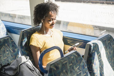 Young woman with earphones using smartphone on a train - UUF19768