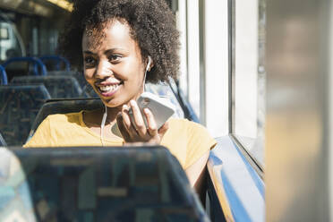 Glückliche junge Frau mit Kopfhörern und Smartphone in einem Zug - UUF19769