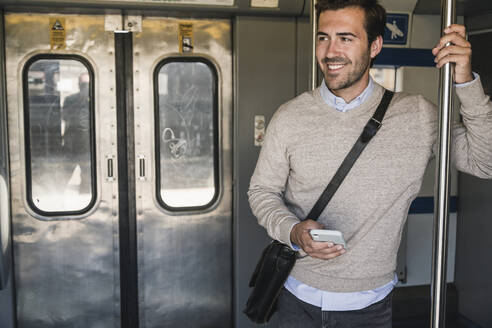 Lächelnder junger Mann mit Smartphone in einem Zug - UUF19778