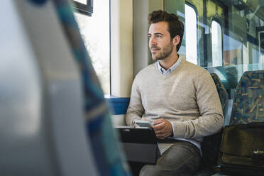 Young man with smartphone and tablet on a train - UUF19779