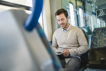 Young man using smartphone and tablet on a train - UUF19780