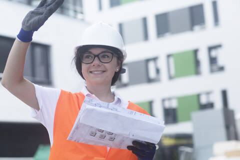 Bauingenieurin mit Bauplan, winkend, lizenzfreies Stockfoto