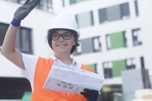 Female construction engineer with construction plan, waving - SGF02559