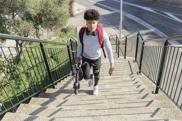 Young man carrying e-scooter on stairs - JPTF00384