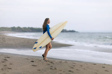 Junge Frau mit Surfbrett am Strand, Kedungu Strand, Bali, Indonesien - KNTF03811