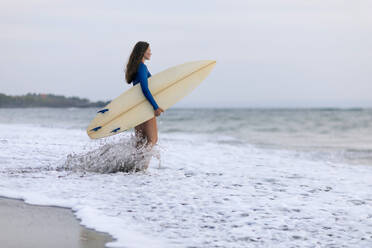 Junge Frau mit Surfbrett am Strand, Kedungu Strand, Bali, Indonesien - KNTF03812