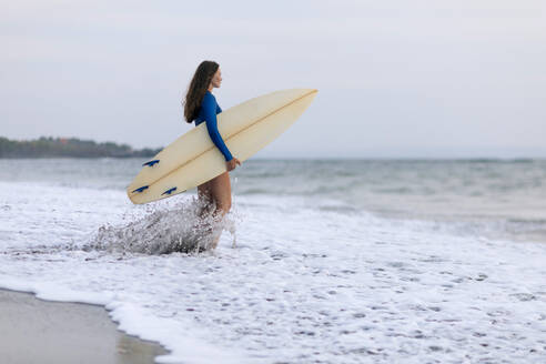 Young woman with surfboard at the beach, Kedungu beach, Bali, Indonesia - KNTF03812