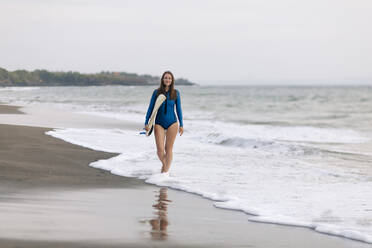 Junge Frau mit Surfbrett am Strand, Kedungu Strand, Bali, Indonesien - KNTF03813