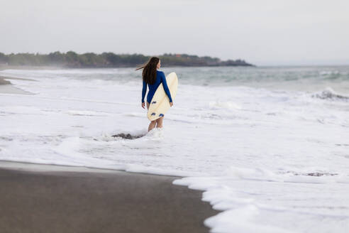 Young woman with surfboard at the beach, Kedungu beach, Bali, Indonesia - KNTF03815