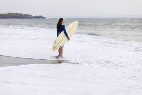 Junge Frau mit Surfbrett am Strand, Kedungu Strand, Bali, Indonesien - KNTF03817