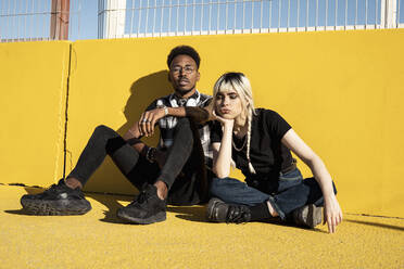 Portrait of young couple sitting in front of yellow wall outdoors - RCPF00156