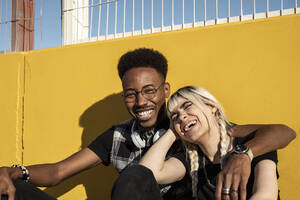 Porträt eines lachenden jungen Paares vor einer gelben Wand - RCPF00157