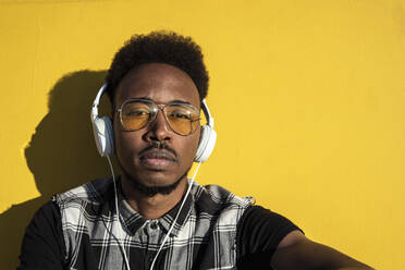 Porträt eines jungen Mannes, der mit Kopfhörern an einer gelben Wand Musik hört - RCPF00180