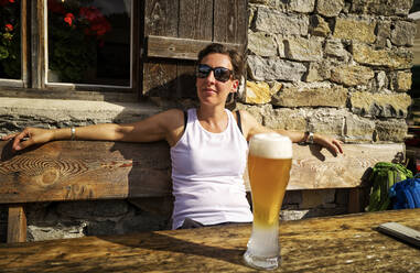 Woman enjoying the sunshine and a wheat beer at a mountain hut, Passeier Valley, South Tyrol, Italy - DIKF00328