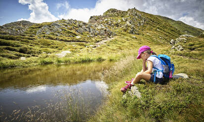 Girl having a break from hiking sitting at a mountain lake, Passeier Valley, South Tyrol, Italy - DIKF00340