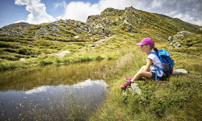 Girl having a break from hiking sitting at a mountain lake, Passeier Valley, South Tyrol, Italy - DIKF00341