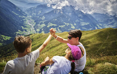 Glückliche Mutter mit zwei Kindern, die eine Pause vom Wandern in alpiner Landschaft machen, Passeiertal, Südtirol, Italien - DIKF00344