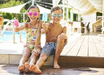 Portrait of happy little girl and boy wearing mirrored sunglasses showing their popsicles - DIKF00359