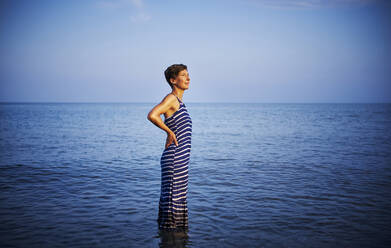Mature woman standing in the sea watching sunset, Italy - DIKF00369