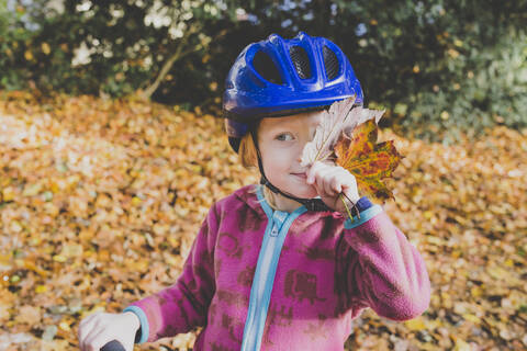 Porträt eines kleinen Mädchens mit Herbstlaub und blauem Fahrradhelm, lizenzfreies Stockfoto