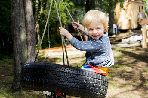 Porträt eines glücklichen Kleinkindes, das auf einer Reifenschaukel sitzt - IHF00226