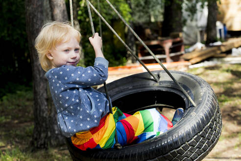 Porträt eines kleinen Mädchens, das auf einer Reifenschaukel sitzt - IHF00227