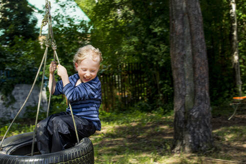 Happy little boy sitting on tire swing - IHF00229