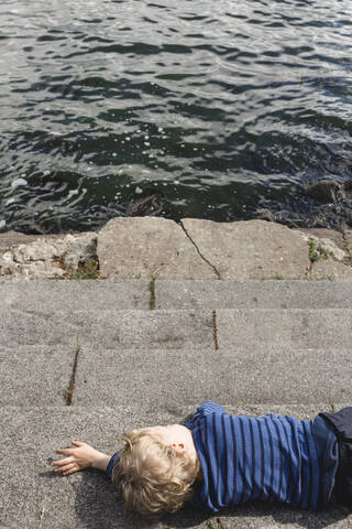 Kleiner Junge ruht sich am Seeufer aus, lizenzfreies Stockfoto
