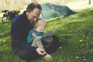 Vater und seine kleine Tochter sitzen zusammen auf einer Wiese mit Karte - IHF00247