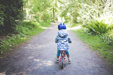 Rückenansicht eines kleinen Mädchens mit blauem Fahrradhelm auf einem Drehgestell - IHF00249