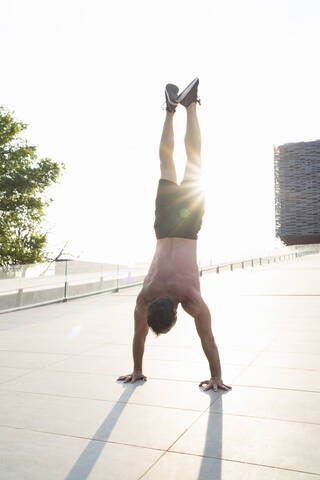 Mann mit nacktem Oberkörper macht bei Sonnenuntergang einen Handstand, lizenzfreies Stockfoto