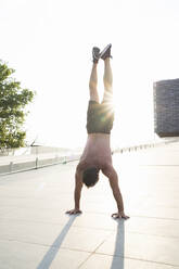 Barechested man doing a handstand at sunset - FBAF01105