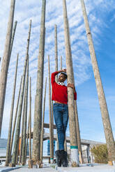 Junger Mann auf Zehenspitzen zwischen Holzpfählen stehend - AFVF04636