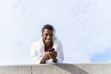 Portrait of happy young man with headphones and smartphone outdoors - AFVF04648