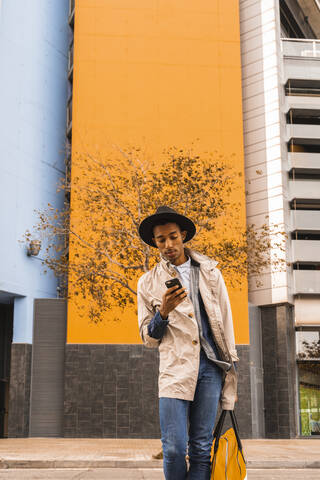 Modischer junger Mann benutzt sein Smartphone im Freien, lizenzfreies Stockfoto
