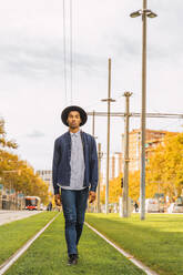 Fashionable young man walking on tram rails - AFVF04676