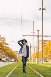 Fashionable young man walking on tram rails - AFVF04677