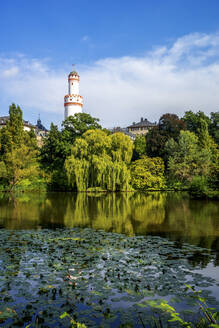 Germany, Hesse, Bad Homburg vor der Hohe, White Tower rising above trees surrounding green lake - PUF01745