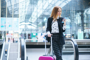 Junge Frau mit Koffer und Mobiltelefon am Bahnhof - KIJF02860