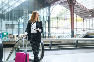Junge Frau mit Koffer und Mobiltelefon am Bahnhof - KIJF02862